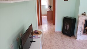 Un passadís estret amb terra de rajola, una paret blanca i una porta de fusta al final.