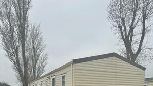 A mobile home with a flat roof, a covered porch, and two propane tanks labeled 'CALOR'. - Family Caravan - Sleeps 6 - Pets Allowed - Pool (King's Lynn)