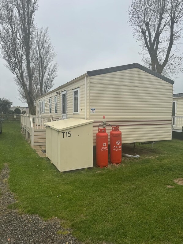 A mobile home with a flat roof, a covered porch, and two propane tanks labeled 'CALOR'. - Family Caravan - Sleeps 6 - Pets Allowed - Pool (King's Lynn)