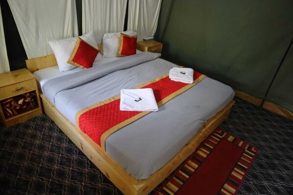 A neatly made bed with white and red linens, a wooden headboard, and a red and yellow striped runner.