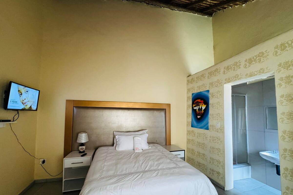 A bedroom with a bed, a nightstand, a TV, and a bathroom visible through an open door.