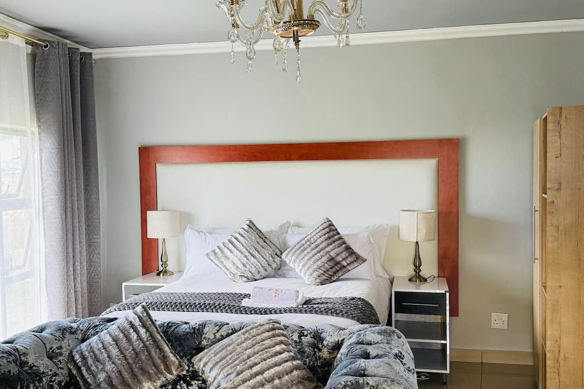A hotel room with a large bed, two bedside tables with lamps, a wooden headboard, and a chandelier.