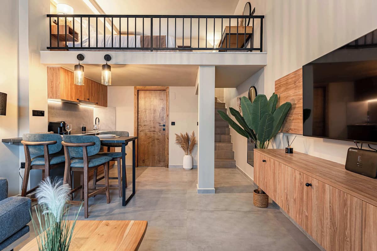 Una cocina moderna con comedor, armarios de madera y una escalera que lleva a un dormitorio tipo loft.