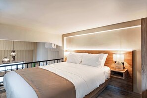 Et moderne hotelværelse med en stor seng, et træhovedgærde, et sengebord med en lampe og udsigt til altanen.