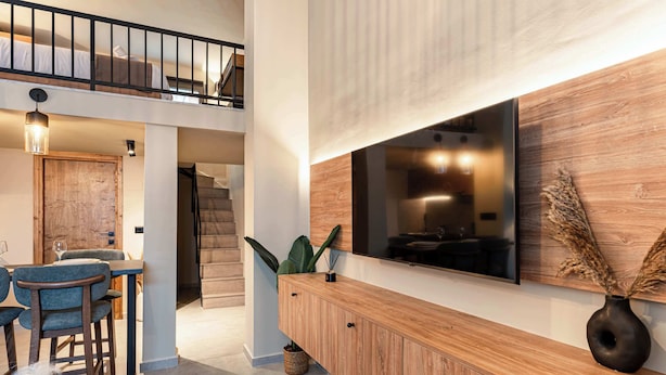 Un interior moderno con comedor, un aparador de madera, un televisor montado en una pared de madera y una escalera que conduce a un nivel superior.