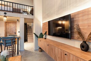 Un interior moderno con comedor, un aparador de madera, un televisor montado en una pared de madera y una escalera que conduce a un nivel superior.
