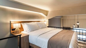 Habitación de hotel moderna con una cama grande, lámpara de noche y vista a la ciudad desde un balcón.