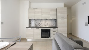 A modern kitchen with light wood cabinets, a marble backsplash, and a built-in oven. - GS Residence (Trani)