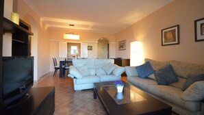 A living room with a sofa, a coffee table, a TV, and a dining area in the background. - LOS CISNES 296 - Three Bedroom Apartment, Sleeps 7 (Punta del moral)