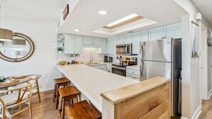 Een moderne keuken met lichtblauwe kastjes, roestvrijstalen apparatuur en een houten bankje.