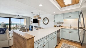 Een moderne keuken met lichtblauwe kastjes, een groot eiland en uitzicht op het strand.