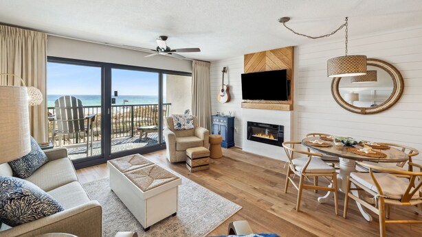 Een ruime woonkamer met een groot raam dat uitkijkt op de oceaan, een open haard en een eethoek met houten meubels.