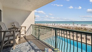 Een balkon met uitzicht op het strand, een zwembad en terrasmeubilair.