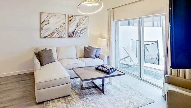 Een moderne woonkamer met een hoekbank, een glazen deur naar een balkon en een marmeren kunstwerk aan de muur.