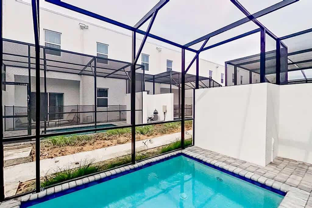 A swimming pool with a glass enclosure, surrounded by a white building with multiple windows.