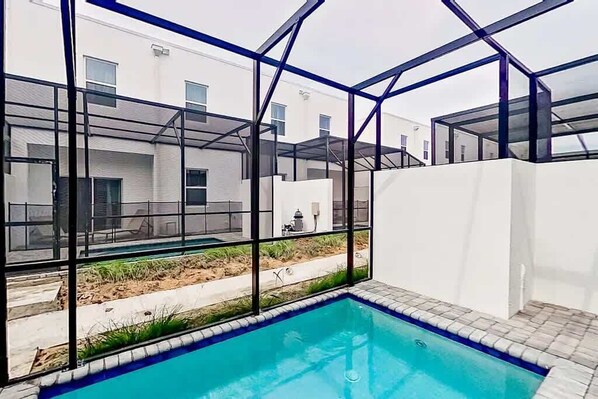 Una piscina con cerramiento de vidrio, rodeada por un edificio blanco con numerosas ventanas.