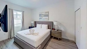 Een moderne hotelkamer met een groot bed, nachtkastjes, een flatscreen televisie en een raam met gordijnen.