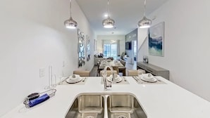 Een moderne keuken met een centraal eiland, een roestvrijstalen spoelbak en hanglampen.