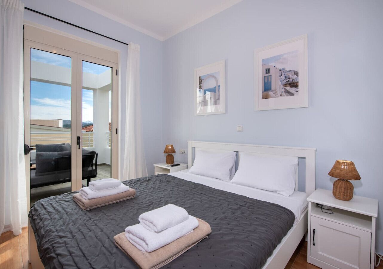 A hotel room with a bed, two bedside tables, a nightstand, a sliding glass door to a balcony, and two framed pictures on the wall.