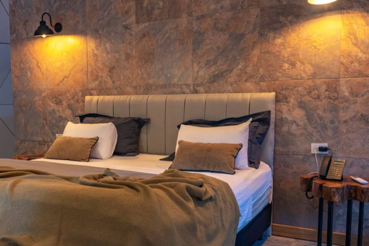 A modern bedroom with a large bed, a bedside table with a phone, and a wall-mounted light fixture.
