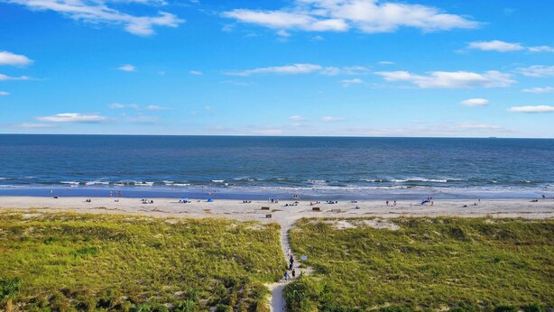 A beach with a clear sky, a sandy shore, and a grassy foreground. - Seaside Sanctuary - Villa Steps from Beach (Hilton Head Island)