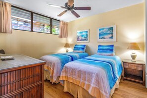 A room with two beds, a desk, a ceiling fan, and two wall-mounted lamps.