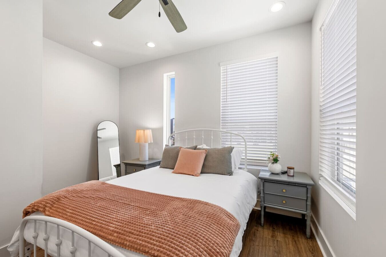 A bedroom with a bed, bedside tables, a lamp, a mirror, and a window with blinds.