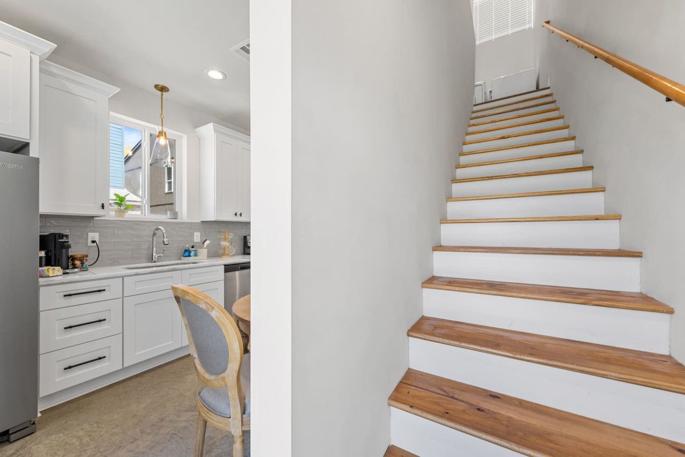 Une cuisine moderne avec des meubles blancs, une chaise en bois et un escalier avec des marches en bois.