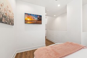 Camera d'albergo moderna con un grande quadro raffigurante un tramonto, un letto con coperta rosa e pavimento in legno.
