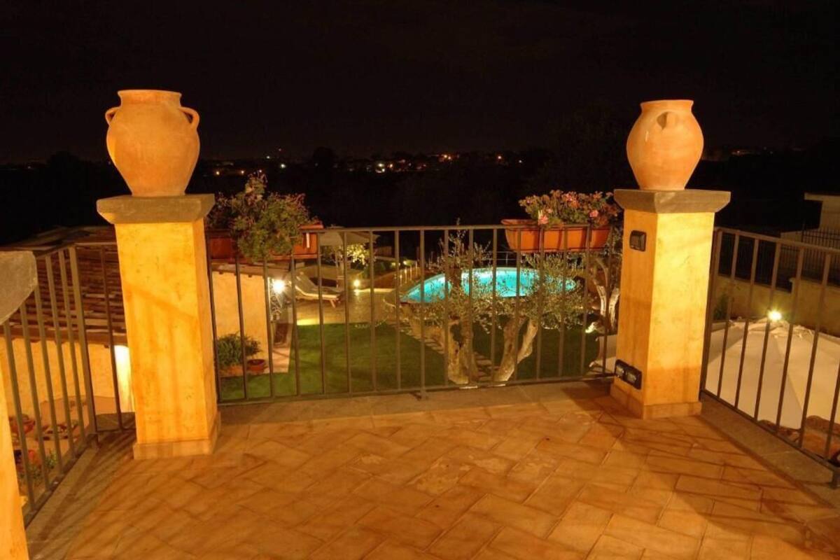 A rooftop terrace with a swimming pool, potted plants, and two large vases on pedestals.