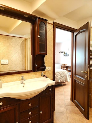 Un bagno con un grande specchio, un lavandino e una porta che dà su una camera da letto.