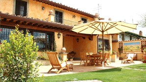 An outdoor patio with a table and chairs, surrounded by a well-maintained lawn and a building with a tiled roof. - La Valle Dei Casali B&B (Rome)