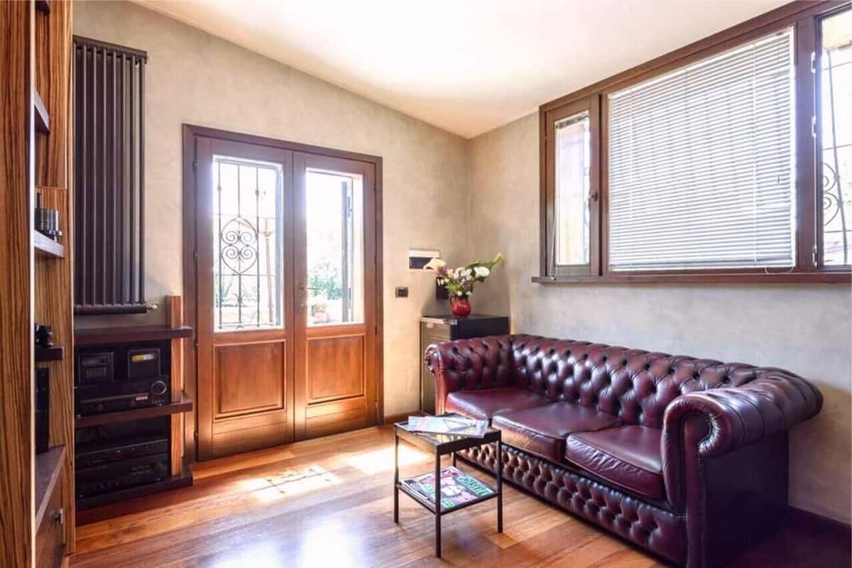 A living room with a leather sofa, wooden entertainment unit, and a window with blinds.