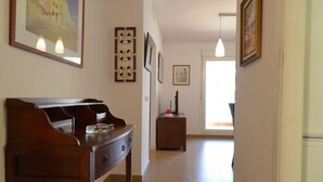 Un couloir avec un piano, des œuvres d’art encadrées, une horloge et un bureau avec un ordinateur.