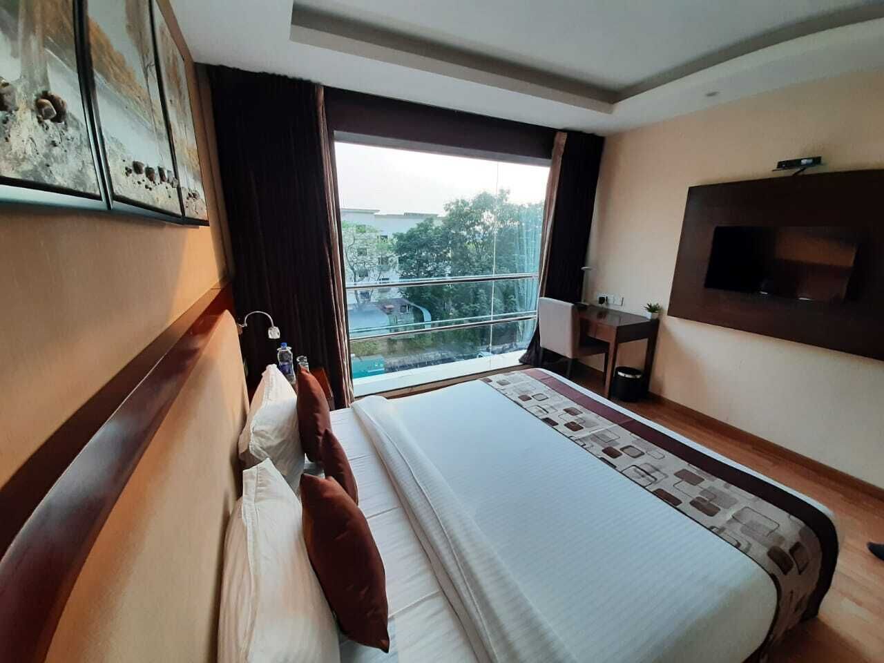 Camera d'hotel con un letto grande, una scrivania, una TV e una finestra vista alberi ed edifici.