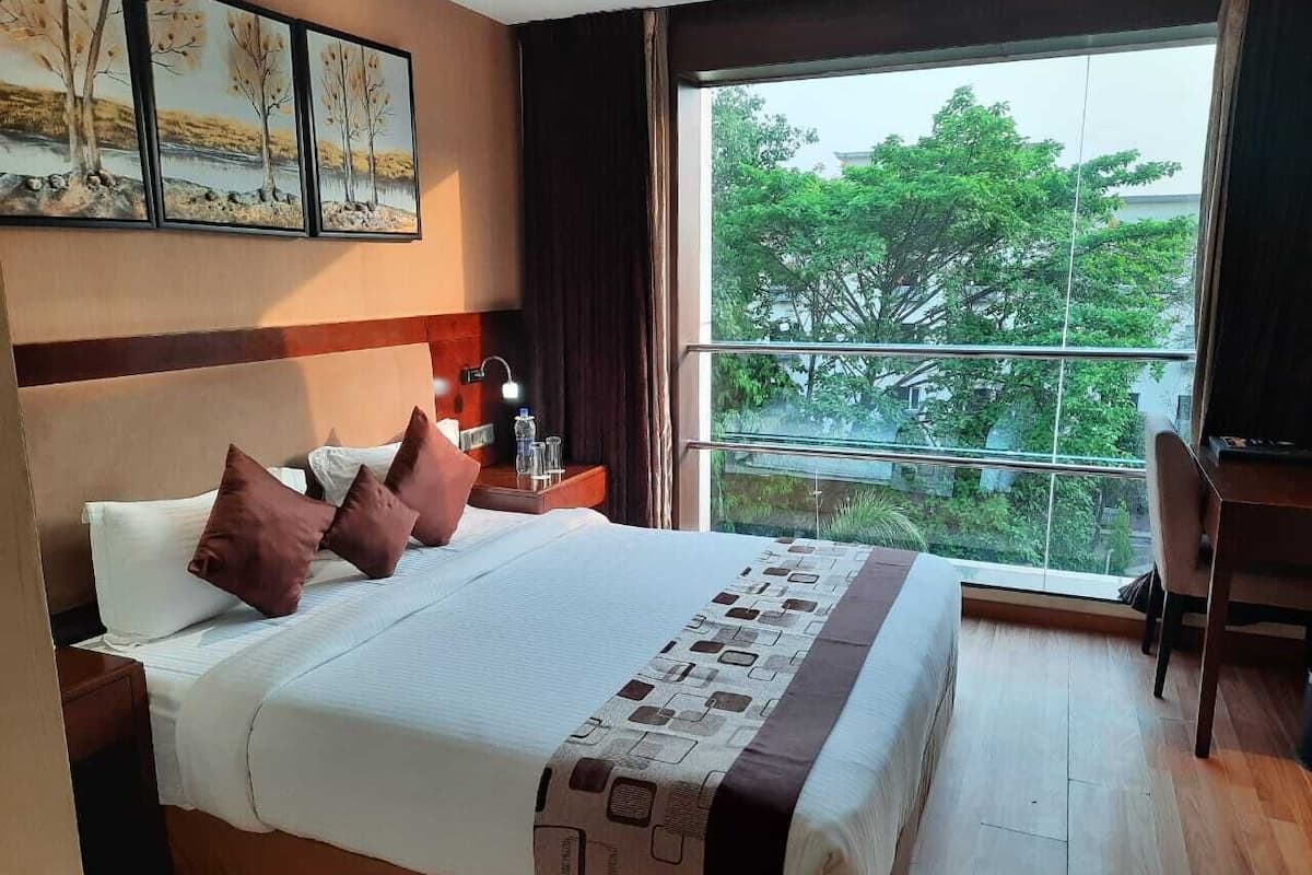 A hotel room with a large bed, a desk, and a view of trees through a window.