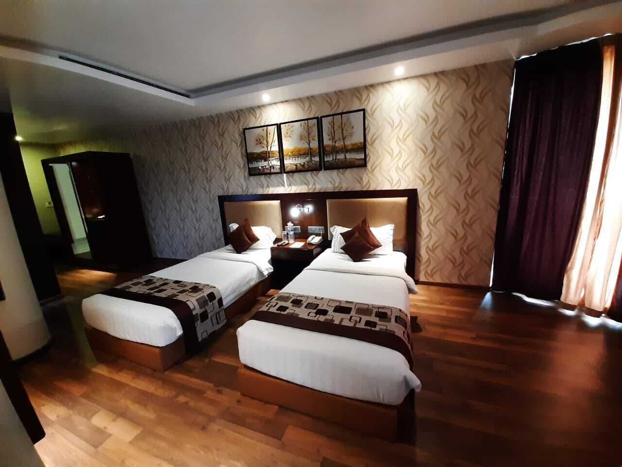 A hotel room with two beds, a headboard with a light fixture, a wall-mounted artwork, and a wooden floor.