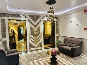 En entréhall med modern design, med ett marmorgolv, en stor kristallkrona och två soffor.