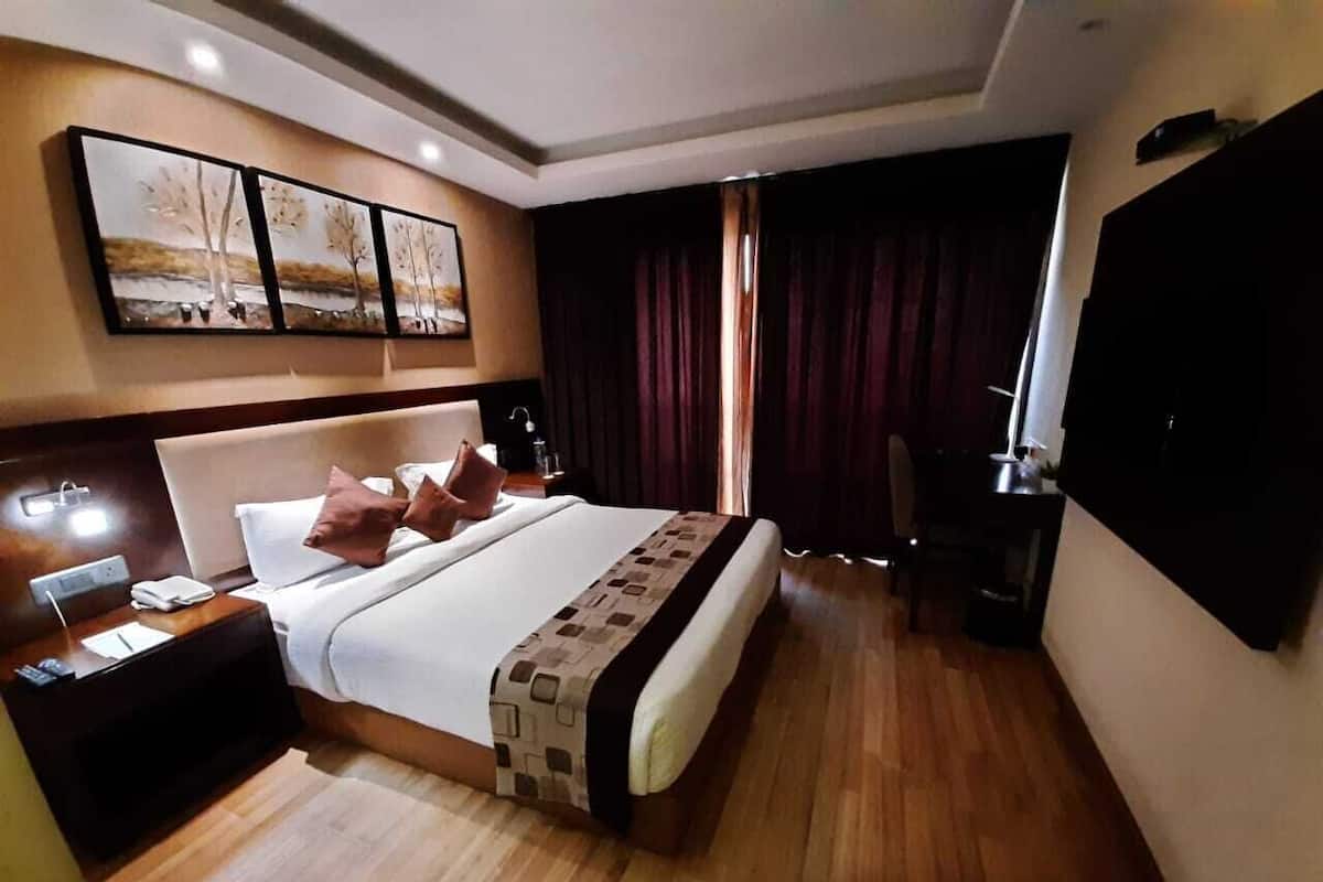 A hotel room with a large bed, a nightstand, a flat-screen TV, and a painting on the wall.