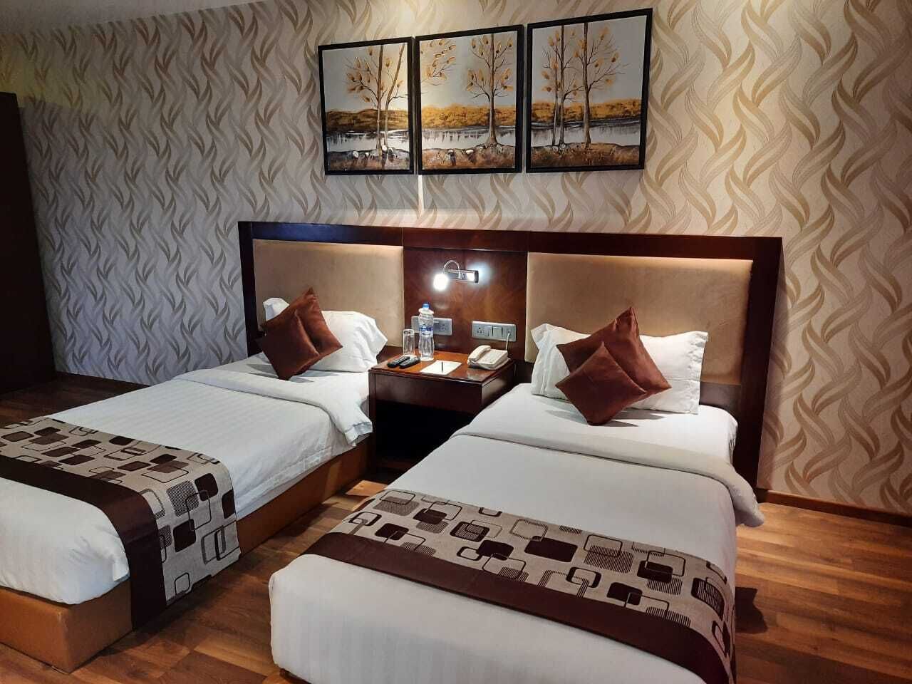 A hotel room with two beds, a nightstand with a lamp, and a wall-mounted picture.