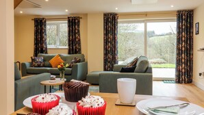 A cozy living room with a green sofa, a coffee table with cupcakes, and a large window with curtains. - Hideaway (Torrington)