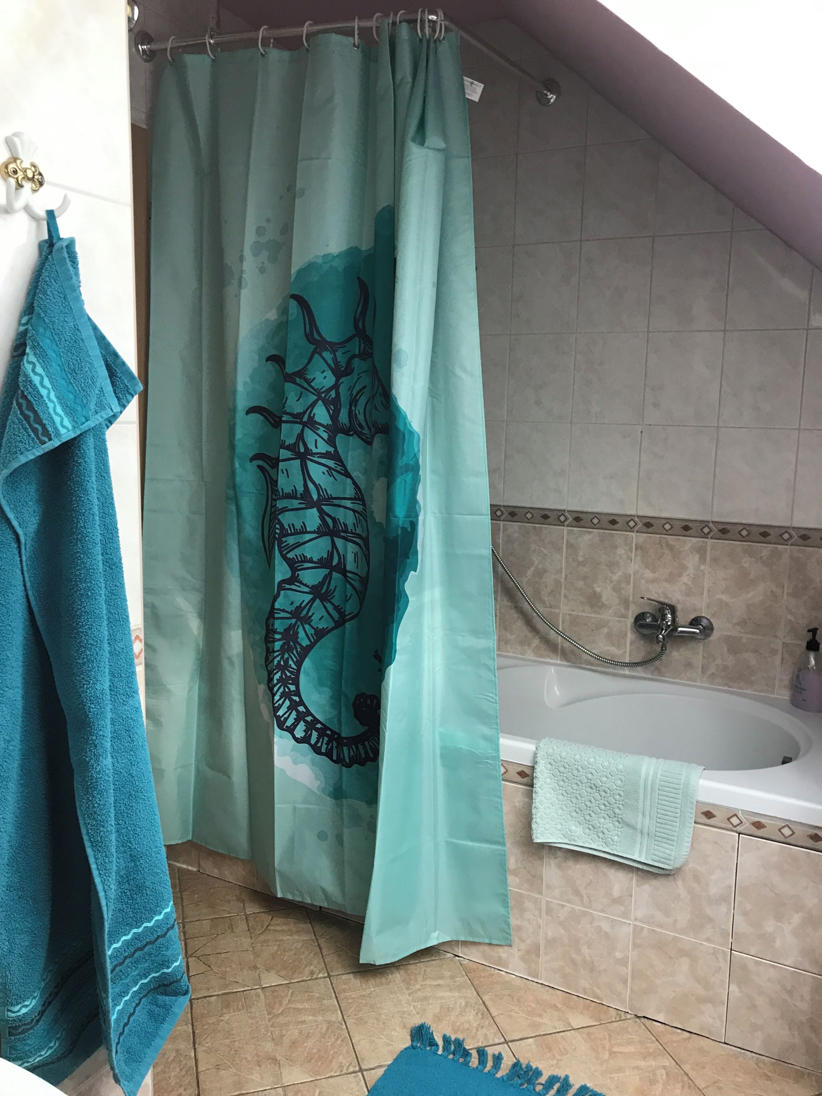 A bathroom with a bathtub, a shower curtain with a seahorse design, and a blue towel on the floor.