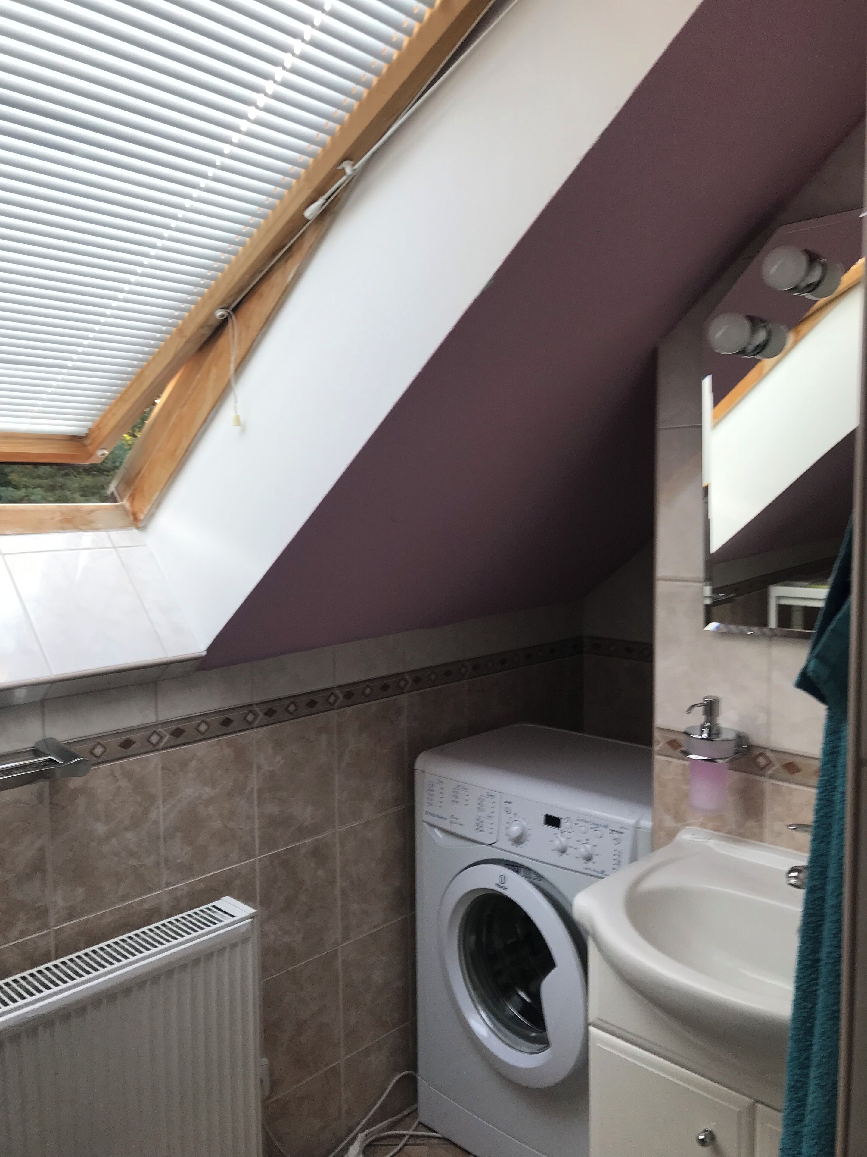 Een kleine wasruimte met een wasmachine, een wasbak en een dakraam erboven.