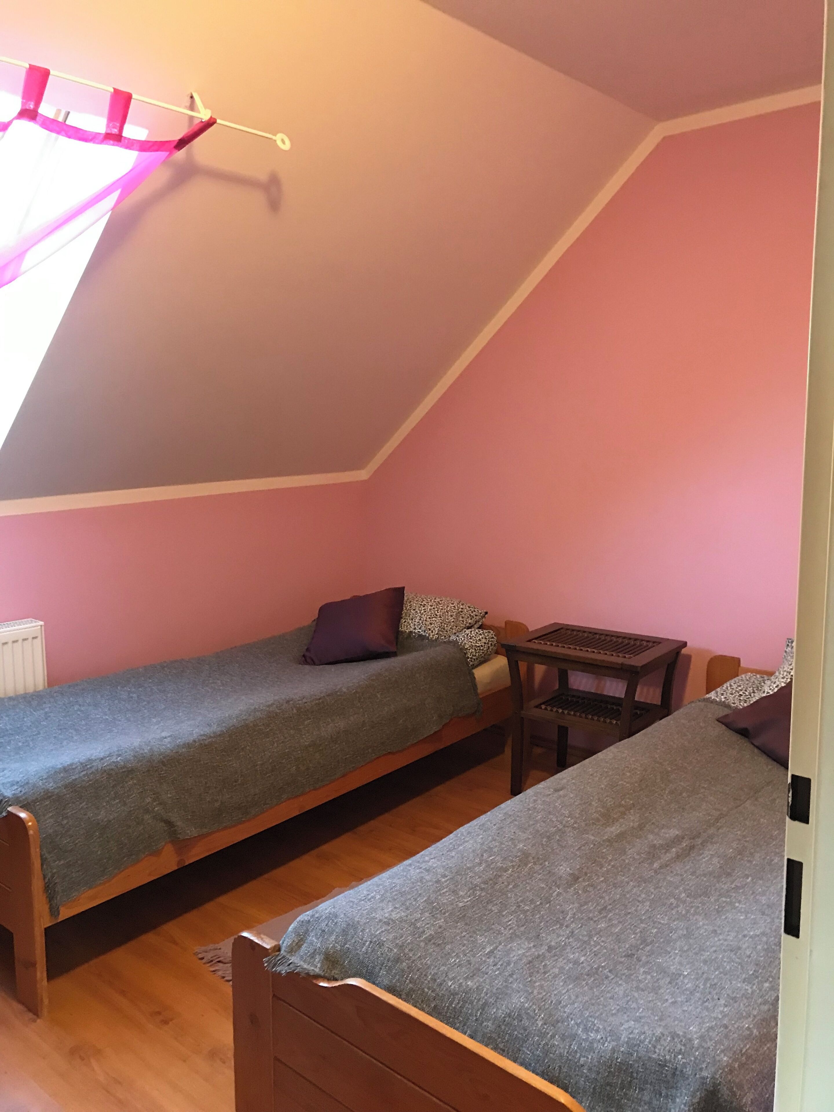 A small, cozy room with two single beds, a wooden table, and a slanted ceiling.