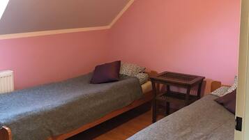A small, cozy room with two single beds, a wooden table, and a slanted ceiling.