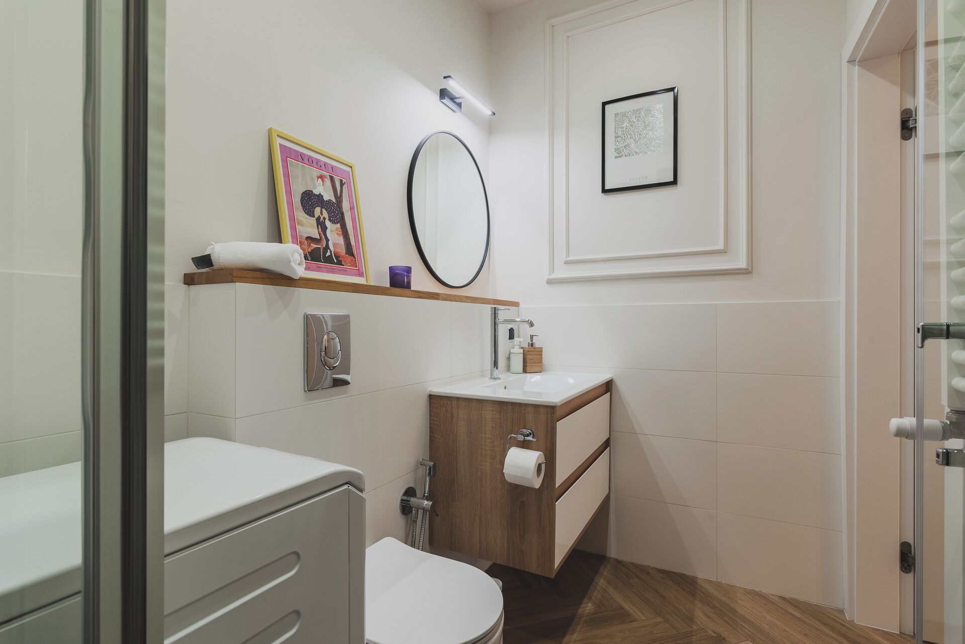 Un baño moderno con inodoro, lavabo y ducha. Hay dos cuadros enmarcados en la pared, una toalla sobre el lavabo y un espejo encima del lavabo.