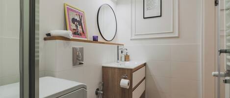 Un baño moderno con inodoro, lavabo y ducha. Hay dos cuadros enmarcados en la pared, una toalla sobre el lavabo y un espejo encima del lavabo.