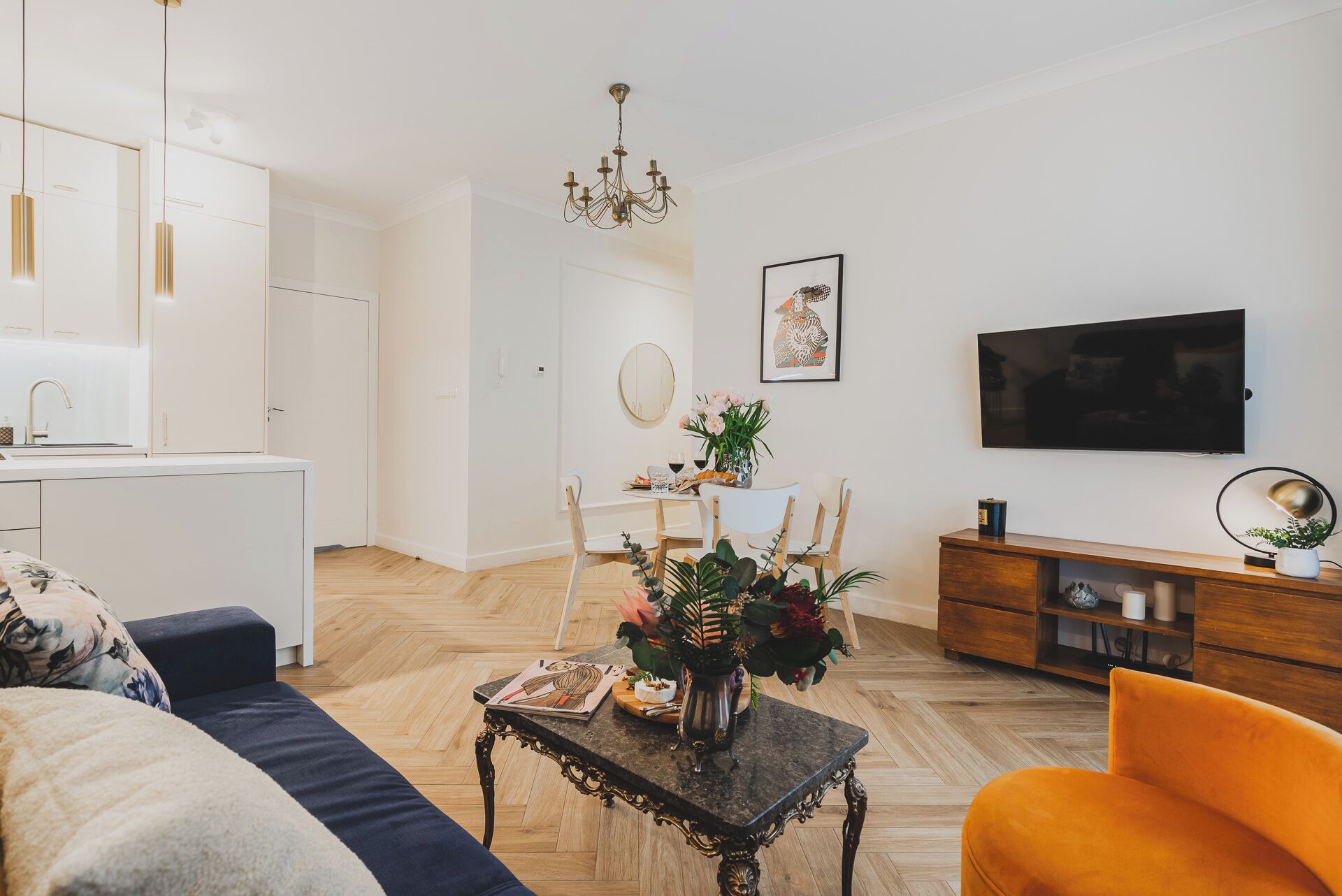 Una sala de estar moderna con un sofá, una mesa de comedor con sillas, un televisor y una araña.