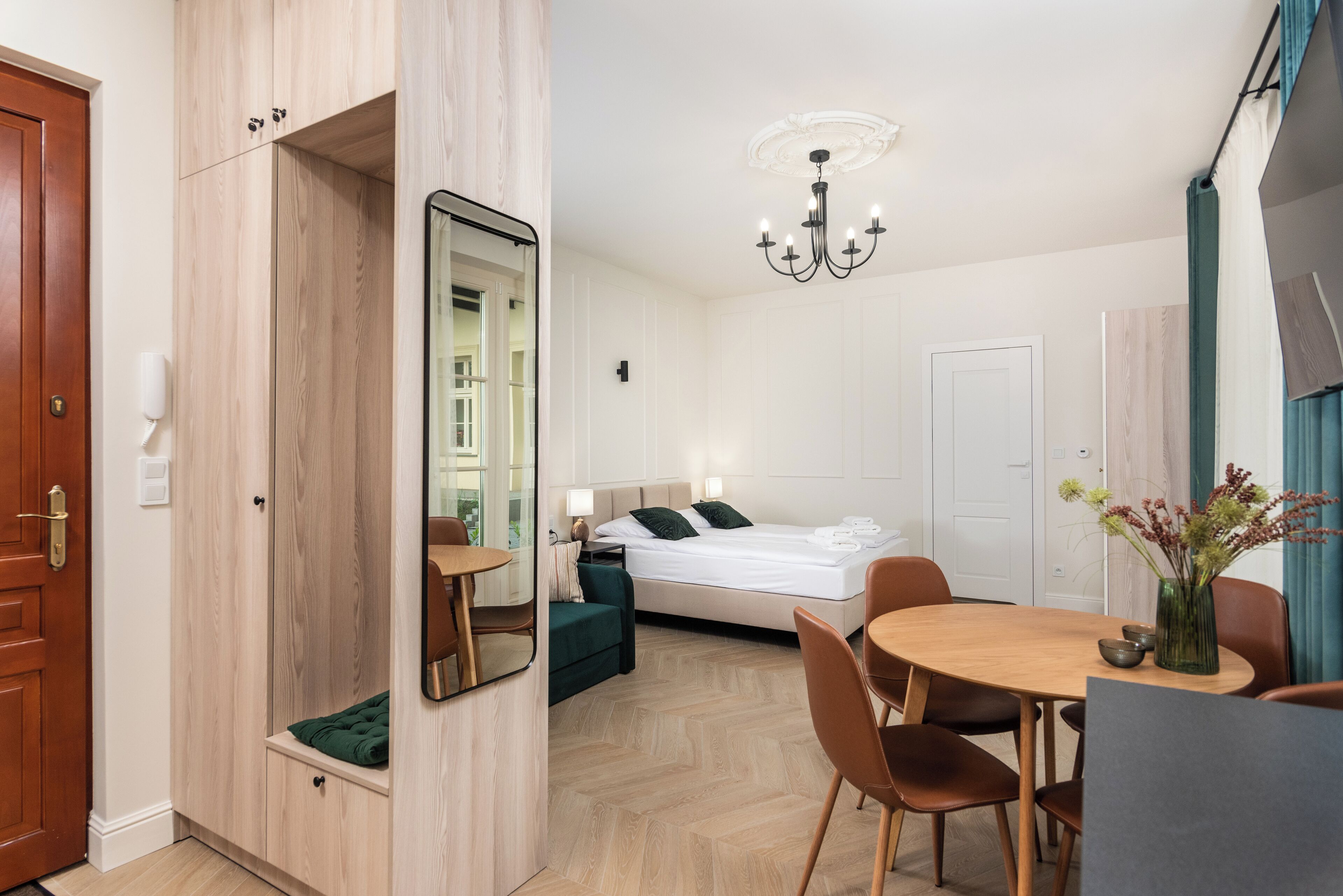 Ein Hotelzimmer mit einem Bett, einem Esstisch mit Stühlen, einem Spiegel, einer Kristallleuchtre und einem Holzschrank.