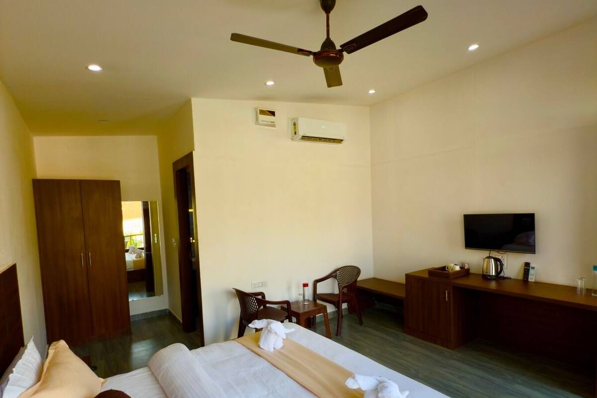 A hotel room with a bed, a desk, a chair, a television, and an air conditioning unit.